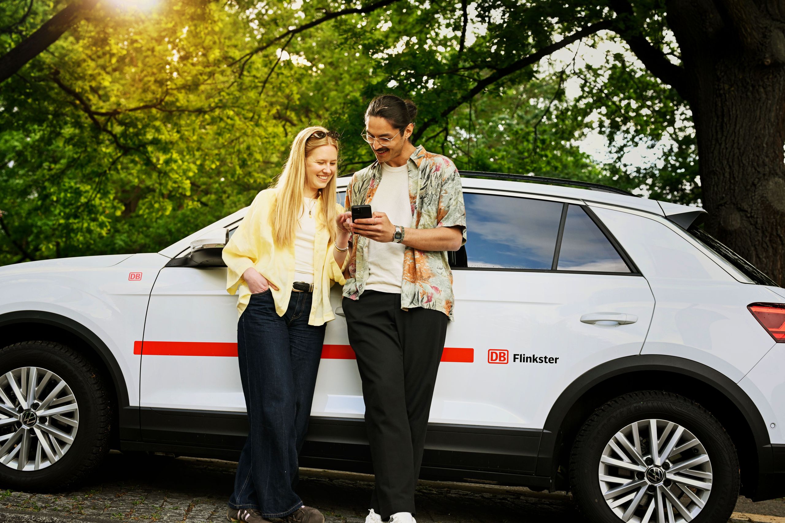 Eine Frau und ein Mann stehen gemeinsam vor DB Flinkster und schauen auf Handy